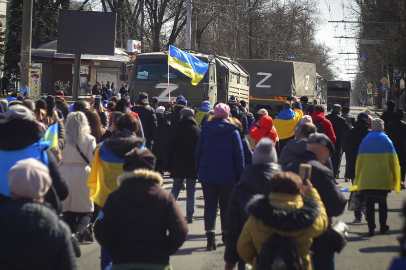 Orang-orang mengibarkan bendera Ukraina selama demonstrasi menentang pendudukan Rusia di Kherson, Ukraina, Sabtu, 5 Maret 2022. Rusia membantu evakuasi penduduk di wilayah Kherson untuk menghindari serangan rudal.