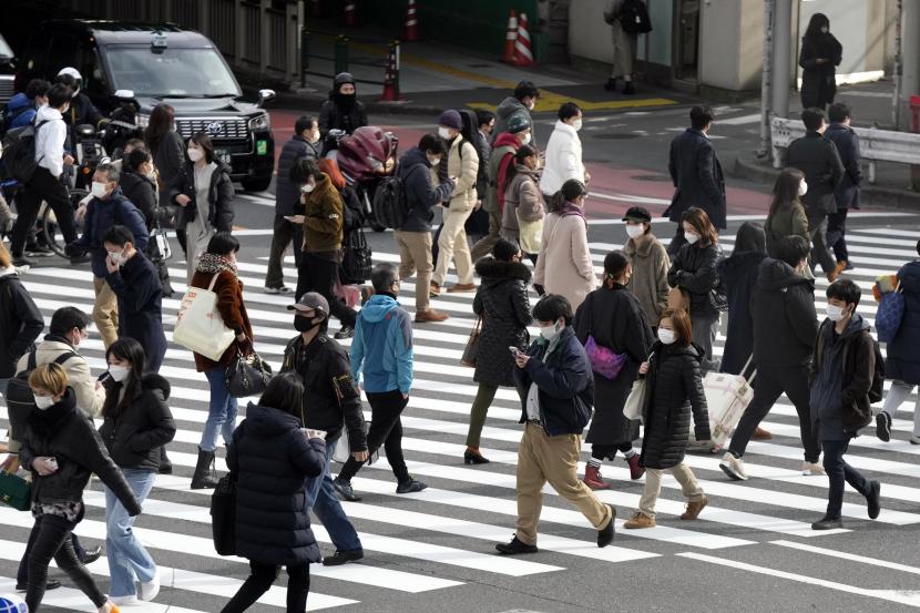 Orang-orang yang memakai masker pelindung untuk membantu mengekang penyebaran virus corona berjalan di sepanjang penyeberangan pejalan kaki Senin, 24 Januari 2022, di Tokyo.