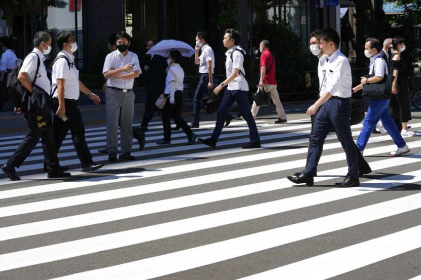 Orang-orang yang memakai masker pelindung untuk membantu mengekang penyebaran virus corona berjalan melintasi penyeberangan pejalan kaki di Tokyo, Jumat, 29 Juli 2022.
