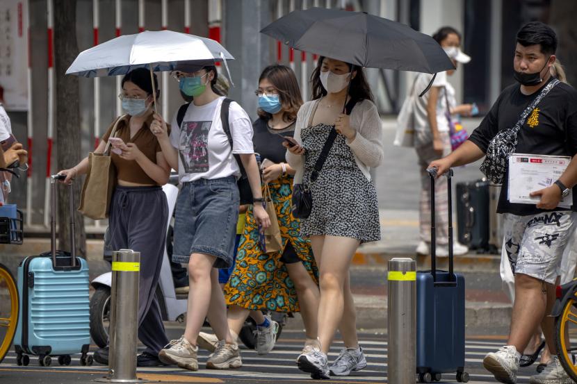 Orang-orang yang memakai masker wajah membawa payung untuk berteduh saat mereka berjalan melintasi persimpangan pada hari yang sangat panas.