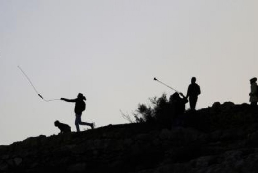 Palestinian protesters use slingshots to throw stones at Israeli troops during clashes near Israel's Ofer Prison, near the West Bank city of Ramallah December 13, 2014. 