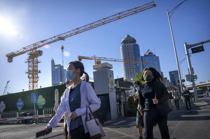 Para komuter yang mengenakan masker berjalan melewati lokasi konstruksi pada jam sibuk pagi hari di Beijing, Selasa, 20 September 2022.