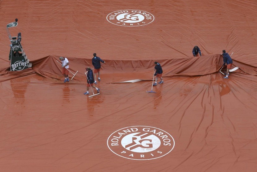 Para pekerja sedang membersihkan lapangan dari acara pembukaan turnamen Prancis Terbuka Roland Garros yang tergenang air