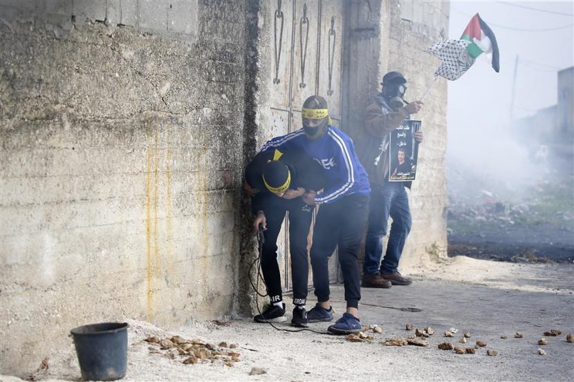  Para pengunjuk rasa Palestina bereaksi terhadap gas air mata selama bentrokan dengan tentara Israel di desa Kafr Qaddum, dekat kota Nablus, Tepi Barat, 23 Desember 2022. Bentrokan itu menyusul protes terhadap permukiman Israel di daerah tersebut. 