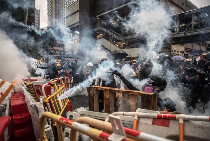 Para pengunjuk rasa yang mengenakan masker gas bereaksi setelah polisi menembakkan gas air mata selama demonstrasi anti-pemerintah di Tsuen Wan, di Hong Kong, Cina, Ahad (25/8).