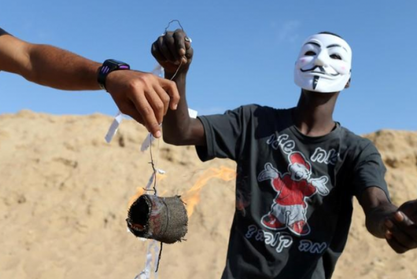 Para remaja Gaza (memakai topeng) menaikkan layang-layang yang membawa bara api dan minyak untuk dijatuhkan di lahan-lahan Israel