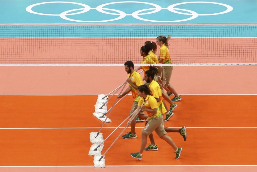 Para sukarelawan Olimpiade Rio sedang mengepel lantai untuk digunakan dalam pertandingan bola voli.