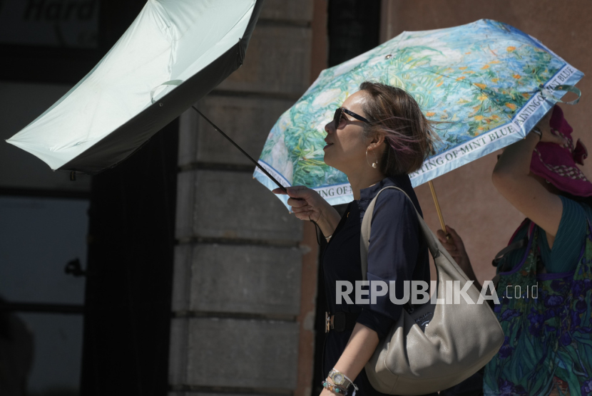 Para wanita berjalan sambil membawa payung untuk berlindung dari terik matahari saat cuaca panas, dekat Castle Square, di Warsawa, Kamis, 3 Juli 2025.
