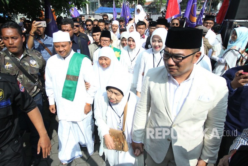 Pasangan calon gubernur dan wakil gubernur Jawa Barat Ridwan Kamil dan Uu Ruzhanul Ulum, berjalan menuntun ibunya menuju massa pendukungnya untuk melaksanakan doa bersama di Lapangan Sidolig, Kota Bandung, Selasa (9/1).