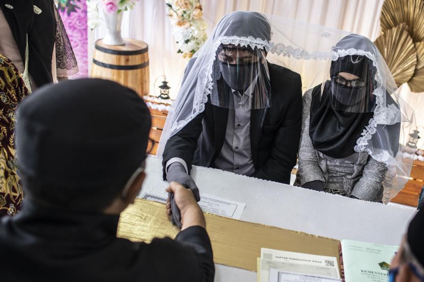 Pasangan pengantin Thomas Rudyanto (kiri) bersama Dian Larasati (kanan) menggunakan sarung tangan, masker, dan pelindung wajah saat melaksanakan prosesi akad nikah di Kantor Urusan Agama (KUA) Ciracas, Jakarta.