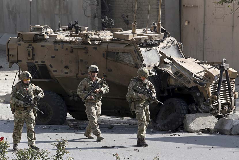 Pasukan NATO berjalan di depan kendaraan militer NATO yang hancur akibat bom bunuh diri di Kabul, Afghanistan, Ahad (11/10).