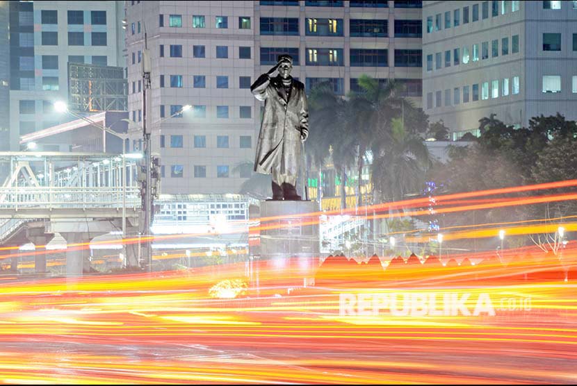 Patung Jenderal Sudirman di timpali Lintasan sinar lampu mobil berpadu dengan lansekap kota malam hari di Jl Jendral Sudirman, Jakarta.