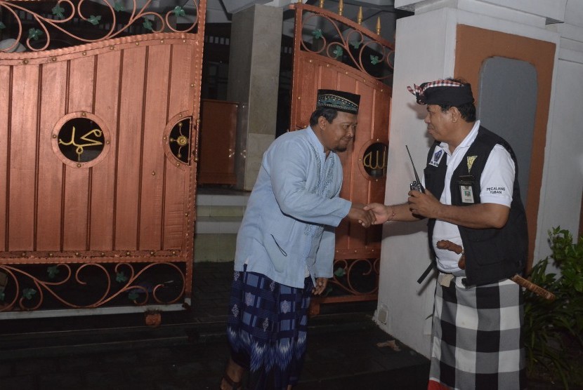 Pecalang atau petugas pengamanan adat Bali berjabat tangan dengan umat muslim yang selesai melakukan Salat Isya berjamaah di Masjid Agung Asasuttaqwa saat melakukan patroli malam di Hari Raya Nyepi Tahun Caka 1941 di wilayah Desa Adat Tuban, Badung, Bali, Kamis (7/3/2019).