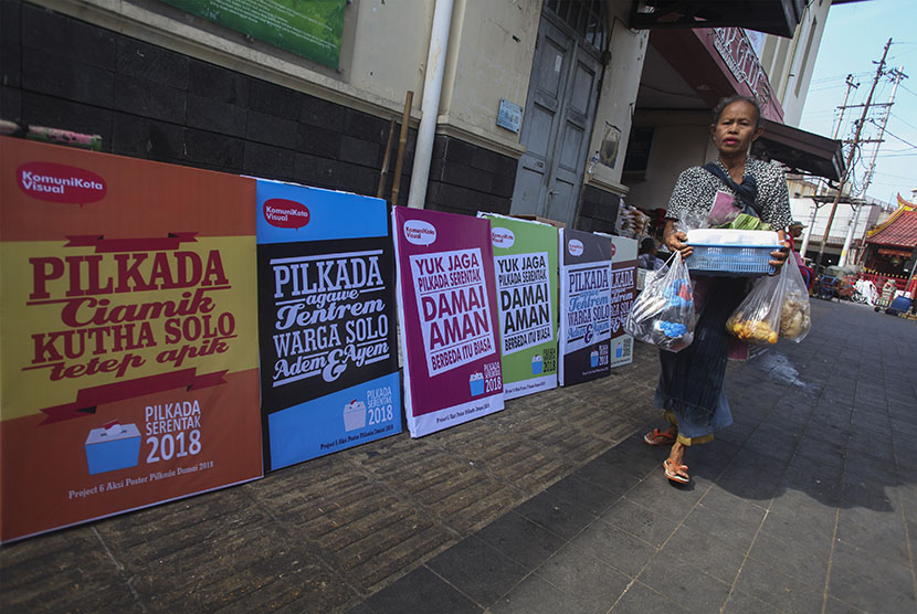 Pedagang melewati jajaran poster Pilkada Damai 2018 yang dipajang di kawasan Pasar Gede, Solo, Jawa Tengah, Senin (25/6). 
