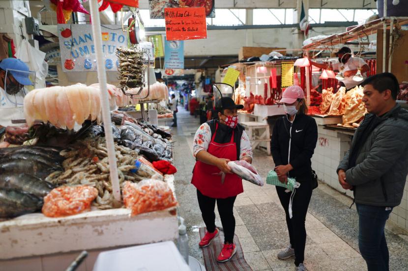 Pedagang membantu pembeli memilih ikan di pasar di Kota Meksiko, Jumat (15/5). Meksiko akan membuka kembali perekonomiannya mulai 1 Juni 2020.