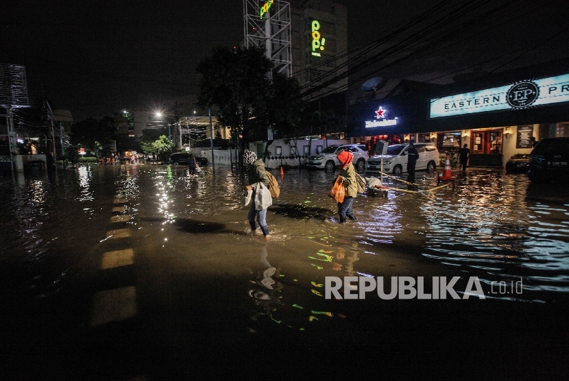 Pejalan berusaha melintasi banjir yang menggenangi kawasan niaga Kemang, Ahad malam (25/9).