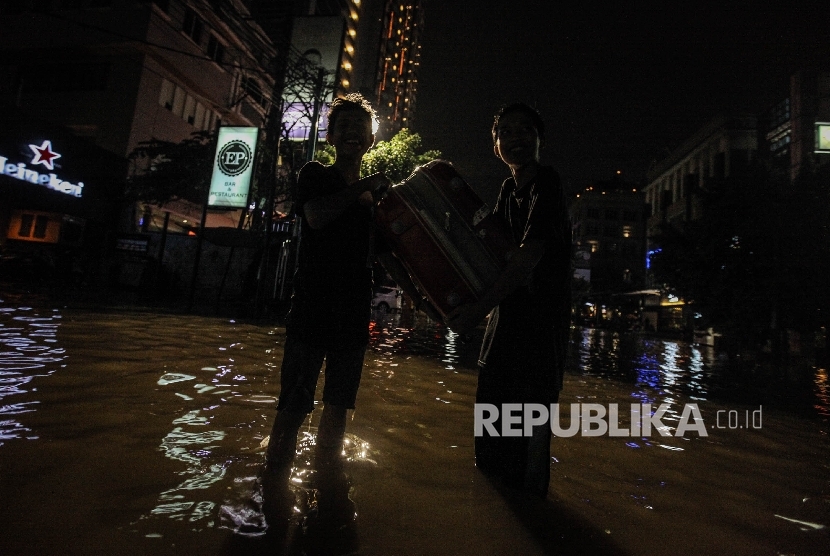 Pejalan berusaha melintasi banjir yang menggenangi kawasan niaga Kemang, Ahad malam (25/9).