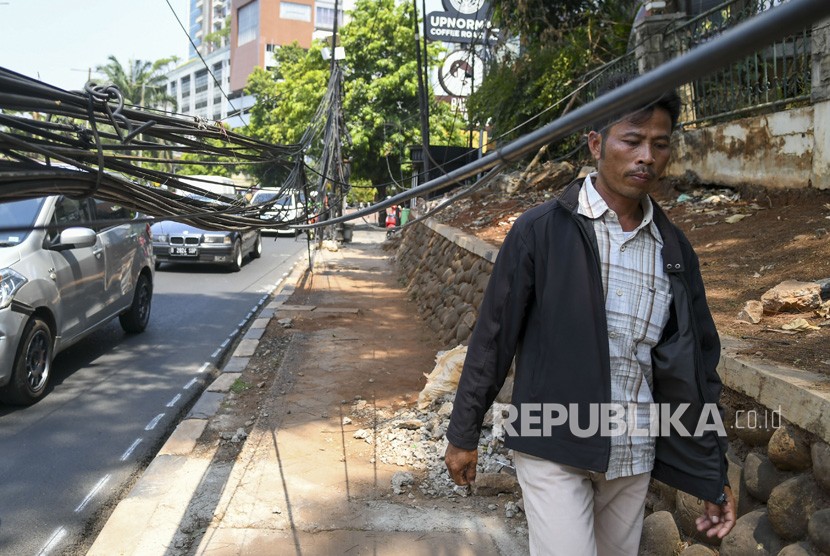 Pejalan kaki melintas di dekat kabel yang terjuntai semrawut di trotoar di Jalan Kemang Raya, Jakarta, Selasa (22/10/2019). 