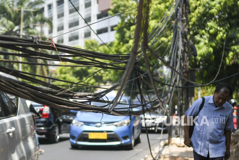 Pejalan kaki melintas di dekat kabel yang terjuntai semrawut di trotoar di Jalan Kemang Raya, Jakarta, Selasa (22/10/2019).