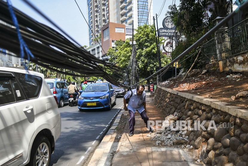 Pejalan kaki melintas di dekat kabel yang terjuntai semrawut di trotoar di Jalan Kemang Raya, Jakarta, Selasa (22/10/2019). 