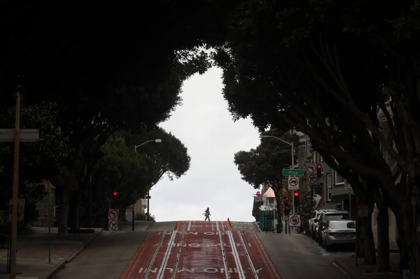 Pejalan kaki melintas di jalanan San Francisco, Amerika, yang sepi akibat keharusan di rumah yang ketat diberlakukan mencegah makin banyaknya korban Covid-19, Ahad (29/3). Covid-19 kini ditemukan di 177 negara dunia.