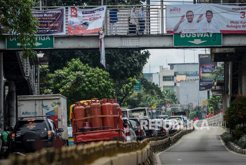 Pejalan kaki melintas di Jembatan Penyeberangan Orang (JPO) yang dipasangi alat peraga kampanye yang telah rusak di Duren Tiga, Jakarta Selatan, Jumat (9/12). 