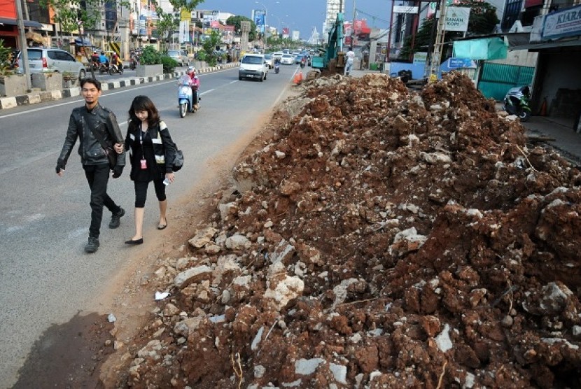 Pejalan kaki melintas di samping tanah galian proyek pembuatan drainase yang belum diangkut di badan jalan Margonda Raya, Depok, Jawa Barat, Selasa (10/12). 