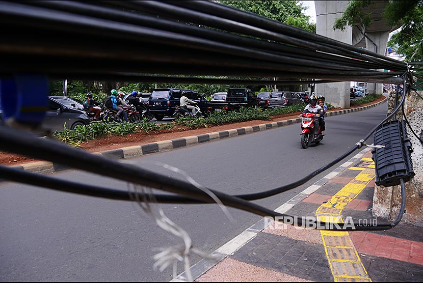 Pejalan kaki melintasi kabel serat optik yang menjuntai di jalan Kyai Maja, Jakarta Selatan, Selasa (19/12). Keberadaan kabel optik di beberapa bagian kota telah mencapai tahap  mengangggu ketertiban dan kenyamanan