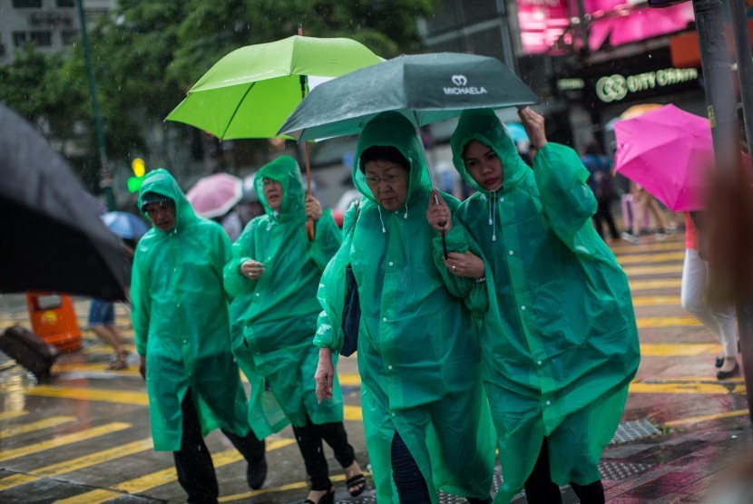 Pejalan kaki mengenakan jas hujan agar terlindung dari hujan deras akibat badai tropis Pakhar yang melanda Hongkong, Cina, pada Ahad (27/8).