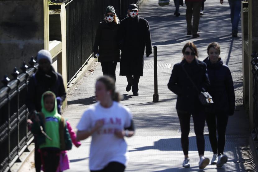 Pejalan kaki mengenakan masker di Regents Park di London, Inggris, Senin (23/3). Pemerintah Inggris mendorong warga jaga jarak satu sama lain untuk menghentikan penyebaran virus corona. 