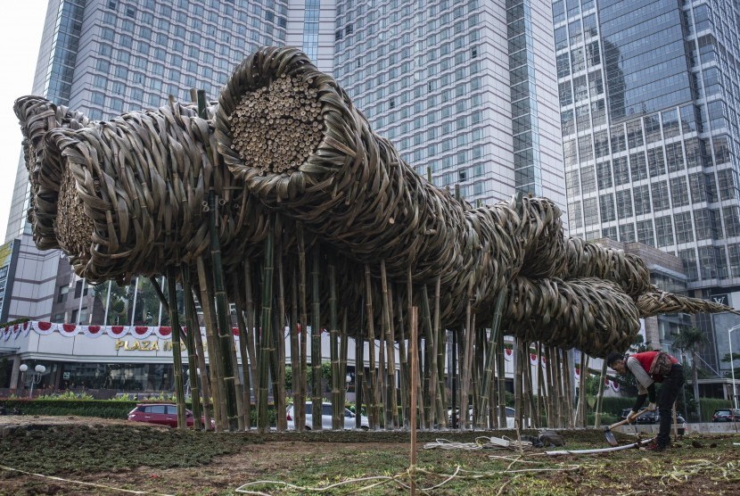Pekerja beraktivitas di dekat karya seni instalasi dari bambu yang dibuat oleh seniman Joko Afianto, di kawasan Bundaran HI, Jakarta, Rabu (15/8). Pemprov DKI Jakarta memasang karya seni tersebut untuk memperindah Jakarta dalam rangka menyambut Asian Games 2018. 