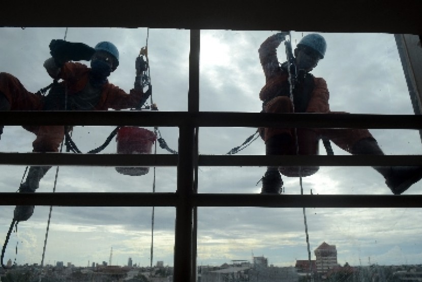 Pekerja bergelantungan dengan tali membersihkan bagian luar sebuah gedung bertingkat.