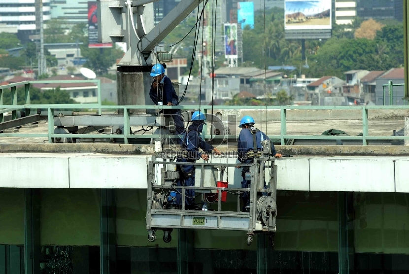 Pekerja dengan perlengkapan keselamatan kerja membersihkan dinding gedung bertingkat di Jakarta, Rabu (29/7). 