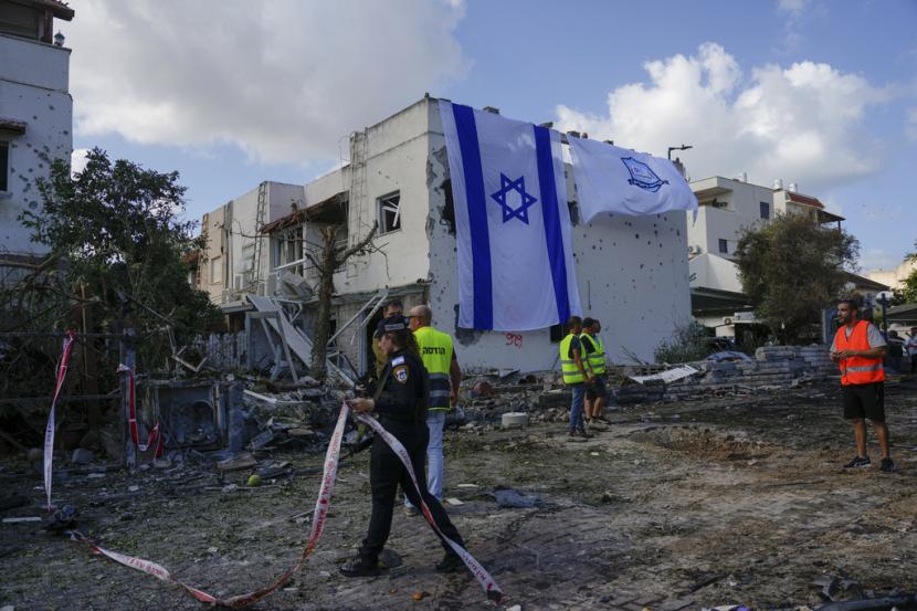 Pekerja kota mengibarkan bendera Israel menutupi bangunan rusak yang terkena roket yang ditembakkan dari Lebanon, di Kiryat Bialik, Israel utara, pada Ahad, 22 September 2024.