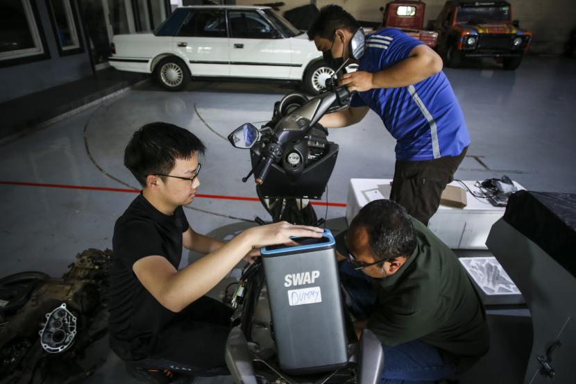 Pekerja memasang baterai saat mengonversi sepeda motor konvensional.