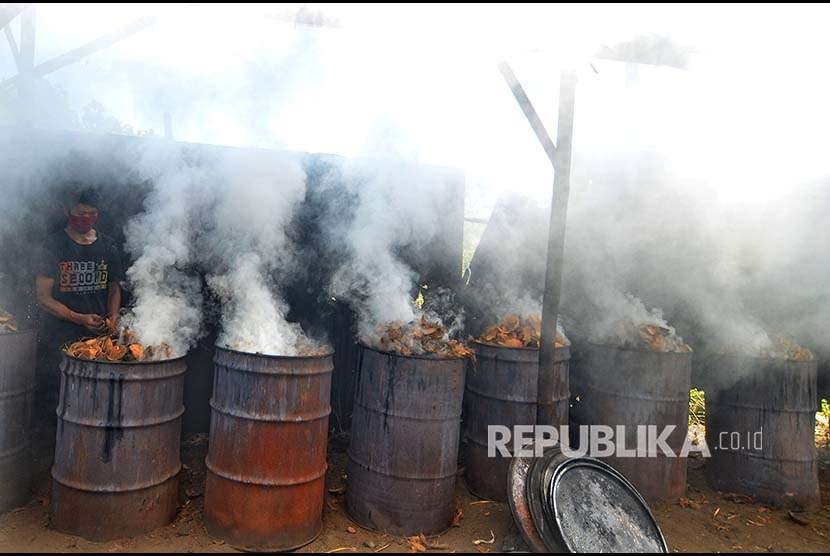Pekerja membakar batok kelapa di dalam tong untuk dijadikan arang.