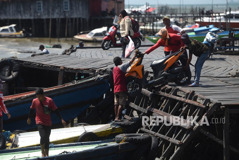 Pekerja menaikkan motor ke atas perahu cepatnya di Pelabuhan Penyebrangan Penajam Paser Utara, Kalimantan Timur.