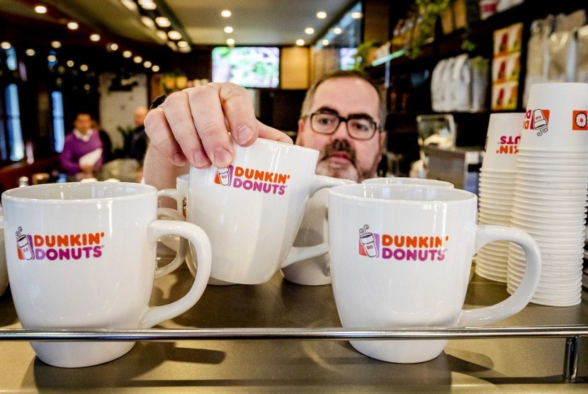 Pekerja menata cangkir minum di gerai Dunkin Donuts.