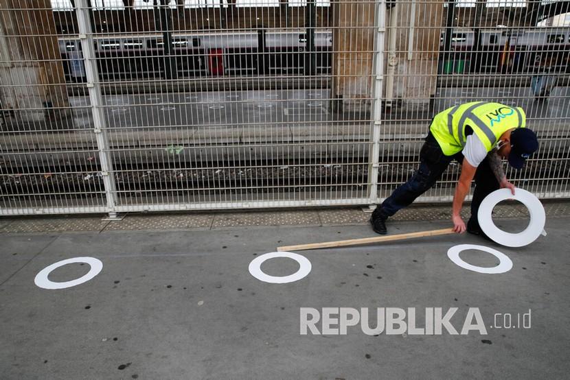 Pekerja menempelkan lingkaran tanda jarak sosial di stasiun kereta Gare du Nord di Paris, Senin (4/5). 