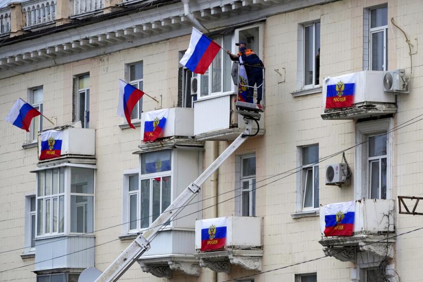 Pekerja menggantung bendera Rusia di sebuah gedung apartemen di Luhansk, Republik Rakyat Luhansk yang dikendalikan oleh separatis yang didukung Rusia, Ukraina timur, Selasa, 27 September 2022. Pemungutan suara dimulai Jumat di empat wilayah Ukraina yang dikuasai Moskow mengenai referendum untuk menjadi bagian dari Rusia .
