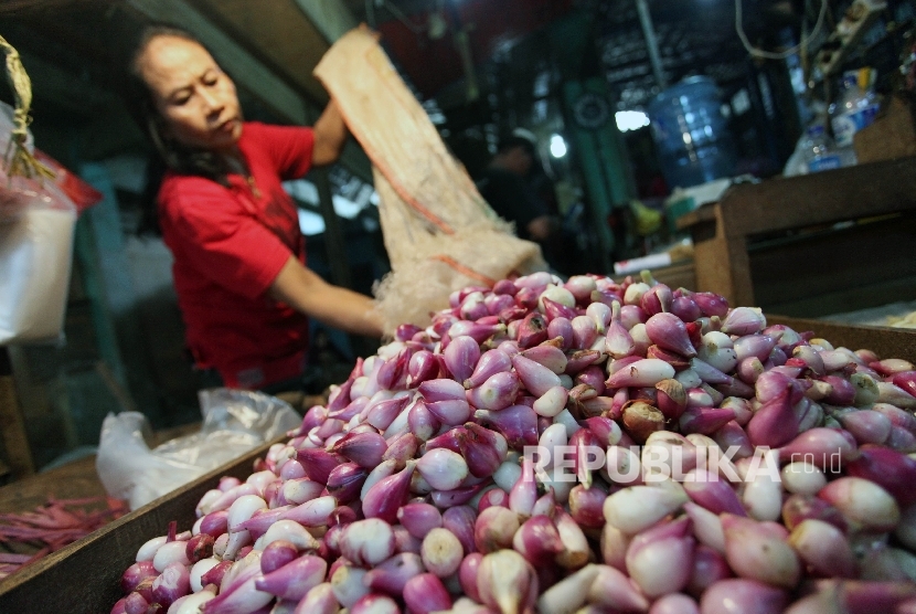 Pekerja mengupas bawang merah di pasar.