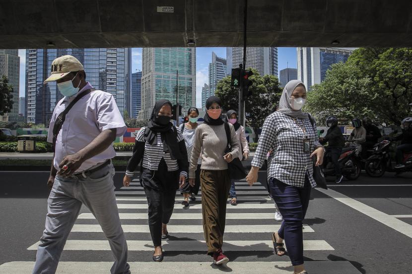 Pekerja menyeberang jalan di kawasan Karet Kuningan, Jakarta, Selasa (22/2/2022). Pemerintah masih memperpanjang PPKM level di luar Jawa-Bali mulai 1-14 Maret. 
