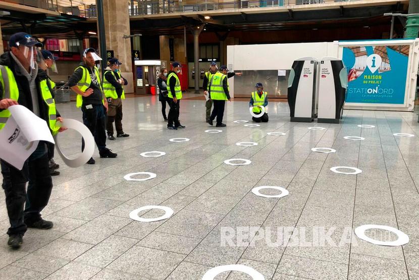 Pekerja menyesuaikan lingkaran yang akan mereka tempel untuk menerapkan jarak sosial di stasiun kereta Gare du Nord di Paris, Senin (4/5). Prancis yang baru menemukan bahwa virus corona ada di negaranya sejak Desember 2019 bersiap untuk melonggarkan lockdown nasional pada 11 Mei. 