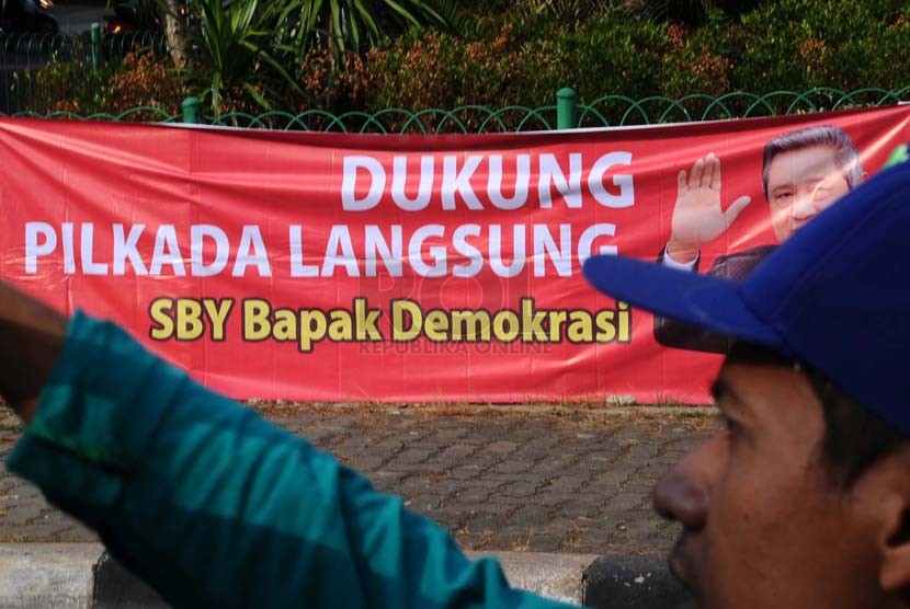 Pekerja sedang membawa selang berlatar belakang spanduk dukungan Pilkada langsung di kawasan Menteng, Jakarta, Senin (22/9).(Republika/ Tahta Aidilla)