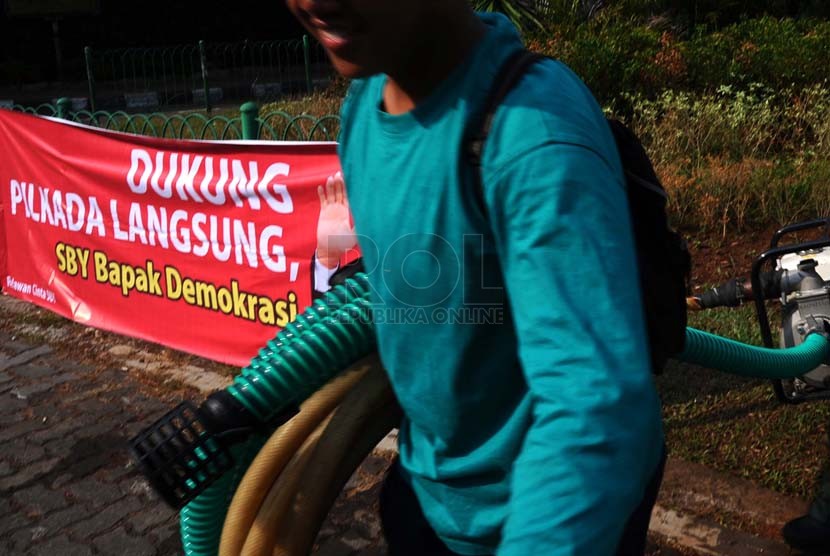 Pekerja sedang membawa selang berlatar belakang spanduk dukungan Pilkada langsung di kawasan Menteng, Jakarta, Senin (22/9).(Republika/ Tahta Aidilla)