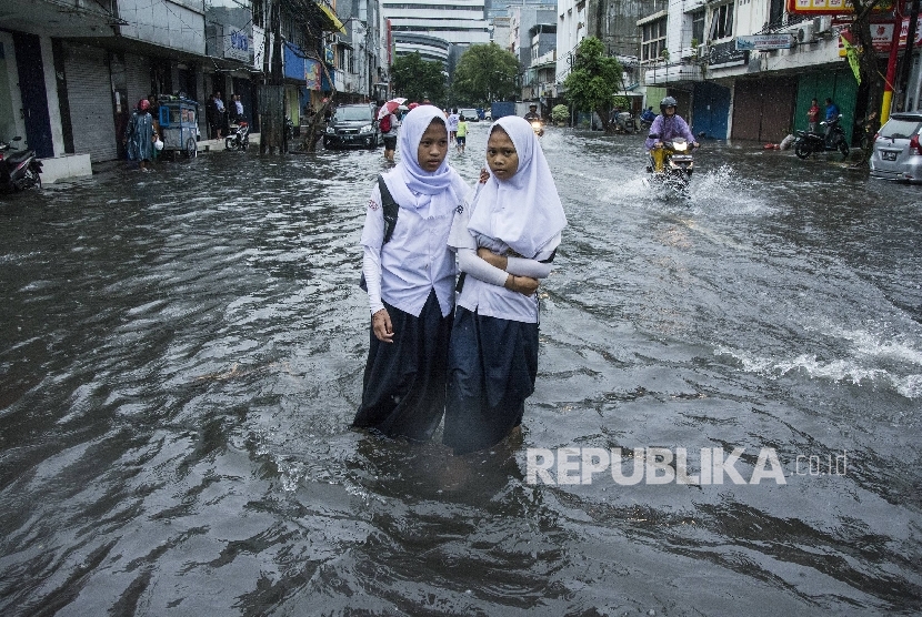 Pelajar berjalan melintasi air banjir di kawasan Sawah Besar, Jakarta, Selasa (21/2).