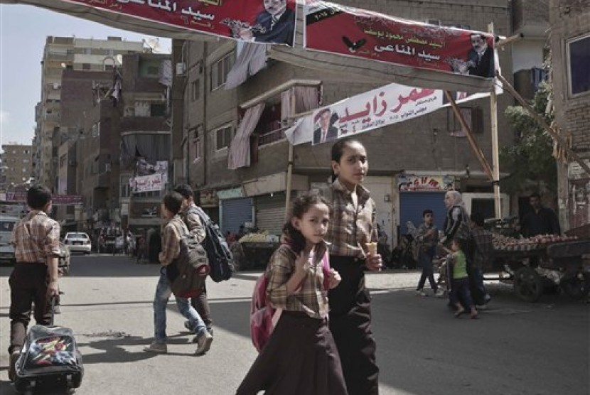 Pelajar Mesir pulang sekolah melewati sebuah spanduk yang memuat foto kandidat anggota parlemen dalam berbahasa Arab di jalan Boulaq El Dakrour di distrik Giza, dekat Kairo, Mesir, Kamis (8/10).