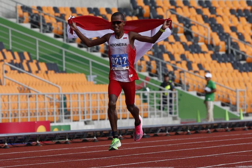 Pelari Indonesia Agus Prayogo mengibarkan bendera Merah Putih saat memasuki garis finis nomor marathon putra SEA Games 2019 di Stadion Atletik New Clark City, Clark, Filipina, Jumat (6/12).