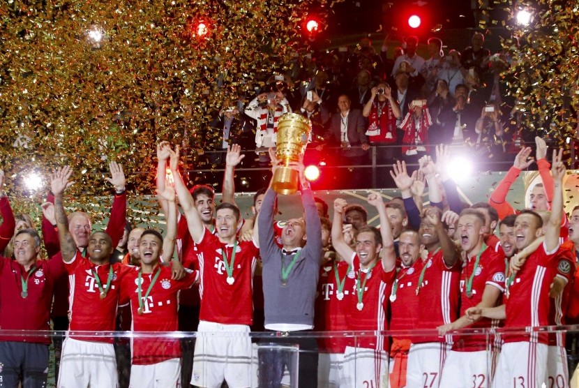 Pelatih Bayern Muenchen Pep Guardiola mengangkat tinggi trofi Piala Jerman usai timnya mengalahkan Dortmund, Ahad (22/5).