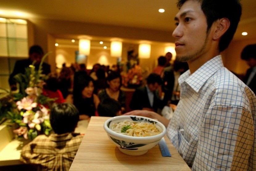 Pelayan restoran membawa udon untuk pelanggan.